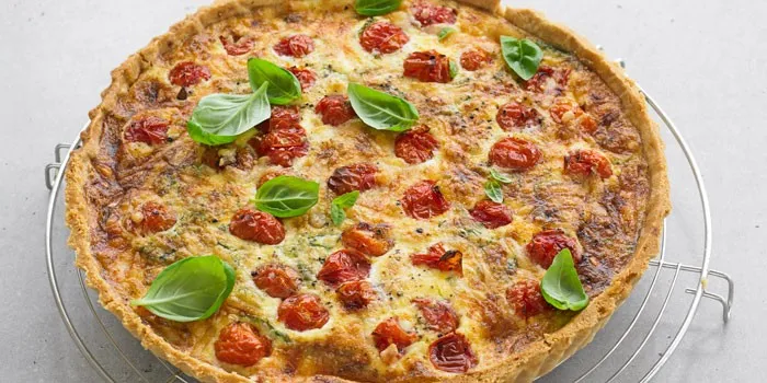 Quiche with tomatoes and basil leaves on rack